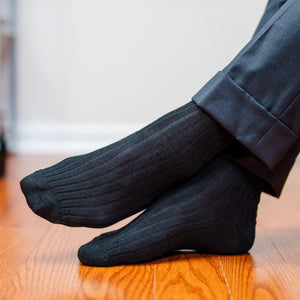 man crossing ankles wearing black ribbed dress socks with charcoal grey trousers