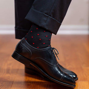 man standing on hardwood floor wearing black dress socks decorated with bright red dots