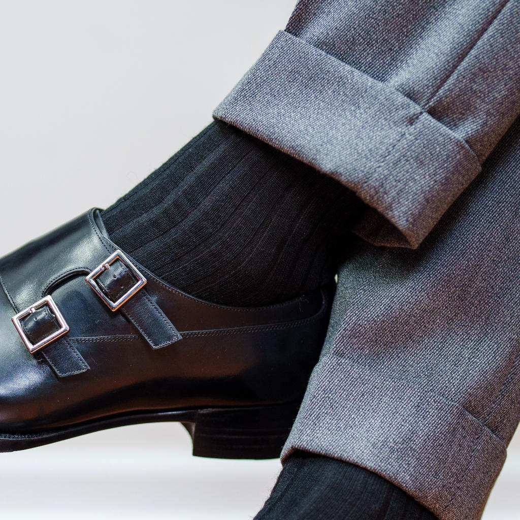 man crossing legs wearing black merino wool ribbed dress socks with a grey suit and black double monkstrap shoes