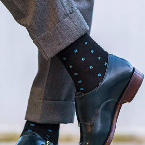 man crossing ankles wearing black dress socks decorated with blue squares