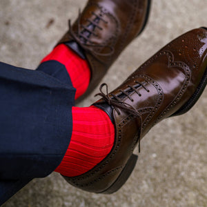 man crossing legs wearing bright red dress socks with navy trousers and dark brown dress shoes