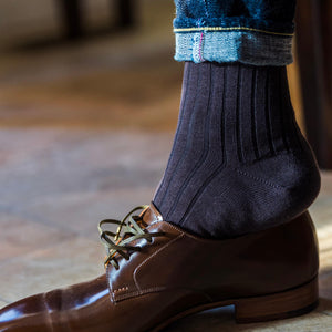 man wearing brown dress socks and jeans sliding foot into dark brown leather dress shoes