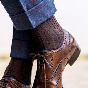 brown dress socks worn by man crossing ankles also wearing blue plaid dress pants and brown dress shoes