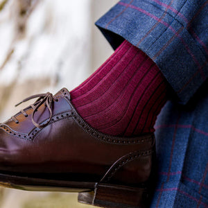 man crossing legs wearing burgundy merino wool dress socks with blue plaid dress pants and brown shoes