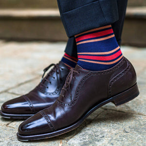 man crossing ankles wearing colorful striped navy dress socks with navy trousers and dark brown dress shoes