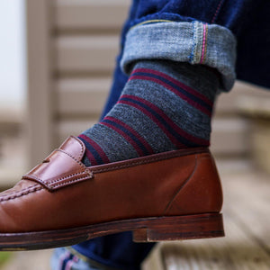man crossing legs wearing heather grey striped dress socks with jeans and brown penny loafers