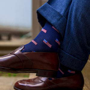 man crossing ankles wearing navy American flag dress socks with navy trousers and brown penny loafers