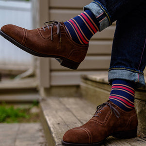 man crossing legs wearing colorful striped dress socks with jeans and brown suede dress shoes