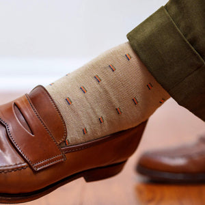 man crossing legs wearing tan patterned dress socks with olive pants and brown penny loafers