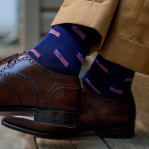 man crossing ankles wearing dark yellow trousers with navy blue American flag dress socks and dark brown oxford brogues