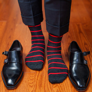 man standing on hardwood floor wearing charcoal grey and red striped dress socks