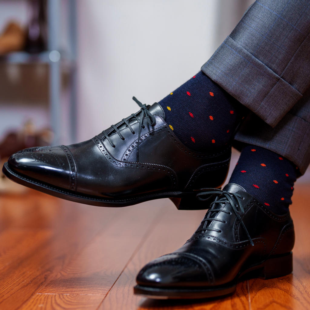 man crossing ankles wearing patterned navy dress socks with black oxfords and a grey windowpane suit