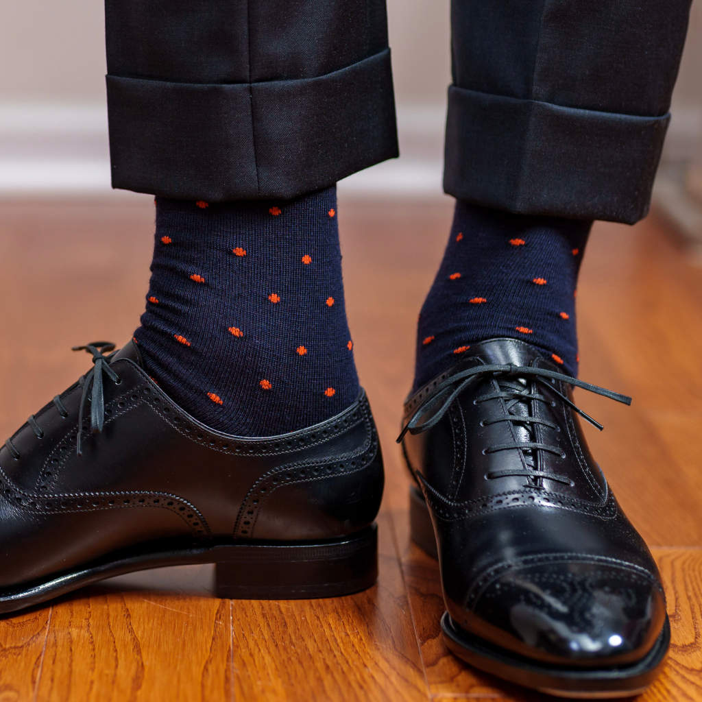 man wearing navy dress socks decorated with bright orange polka dots standing on hardwood floor