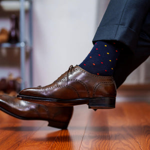 man crossing legs wearing charcoal grey suit with colorful navy dress socks and brown wingtips