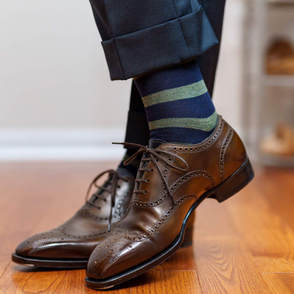 man crossing ankles wearing navy wool dress socks with horizontal olive green stripes