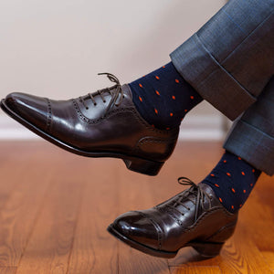 man crossing legs wearing navy and orange patterned dress socks with dark brown oxfords and light grey trousers