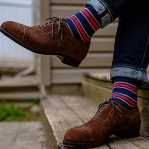 man crossing legs wearing navy dress socks with colorful stripes