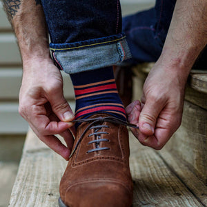 man tying shoes wearing colorful striped dress socks and dark wash jeans