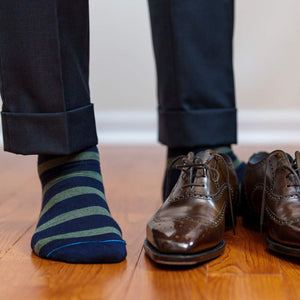 man standing wearing olive and navy dress socks with charcoal trousers and brown oxfords