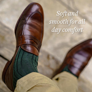 man crossing legs wearing olive green cotton dress socks with brown penny loafers and khaki chinos