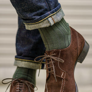 olive green men's dress socks paired with dark wash blue jeans and brown suede dress shoes