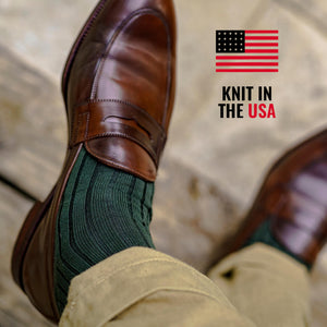 man wearing olive green ribbed dress socks and brown penny loafers with khaki chinos while crossing legs
