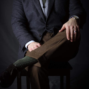 man crossing legs wearing olive green dress socks and brown dress pants with a coat and tie