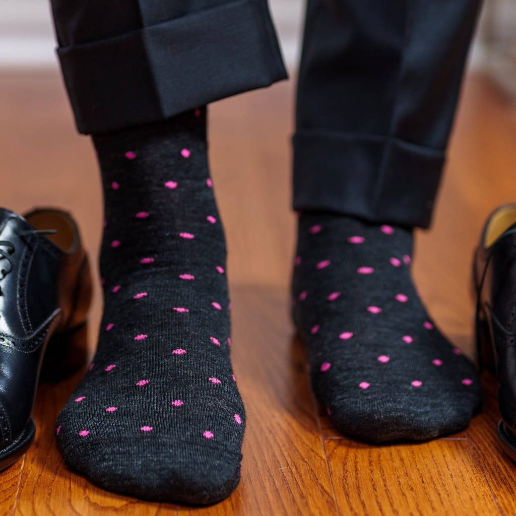 man standing on hardwood floor wearing charcoal grey dress socks decorated with bright pink polka dots