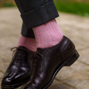 man crossing ankles wearing pink dress socks and grey trousers with dark brown shoes