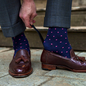 man wearing navy dress socks decorated with bright pink polka dots using shoe horn to put on brown tassel loafers