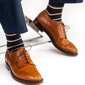 man seated wearing navy trousers and light brown dress shoes with dark grey and pink striped dress socks