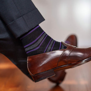 man crossing legs wearing black and purple striped dress socks with penny loafers and charcoal grey trousers