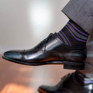 man crossing legs wearing black dress socks with purple and grey stripes