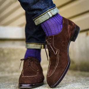 man crossing ankles wearing purple dress socks with dark jeans and brown suede dress shoes