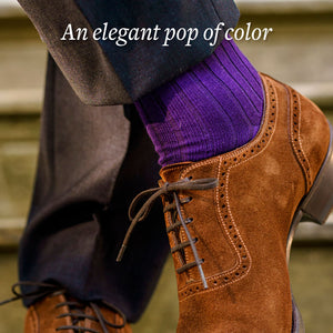 man crossing ankles wearing purple cotton dress socks with grey trousers and brown suede shoes