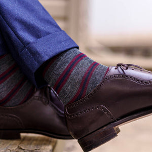 man sitting on steps wearing heather grey dress socks with burgundy and navy stripes